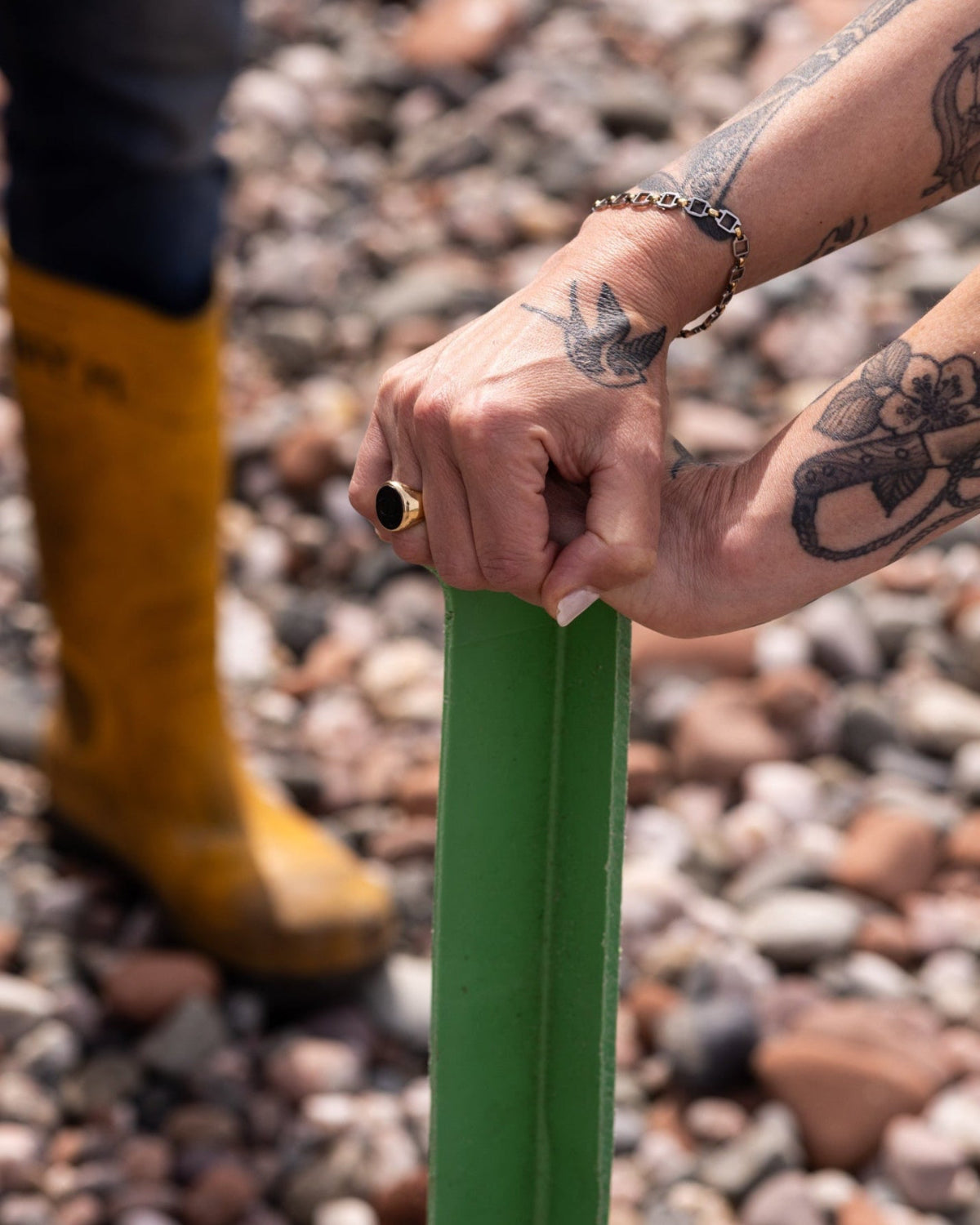 Person wearing yellow boots and holding a green fish box on a beach